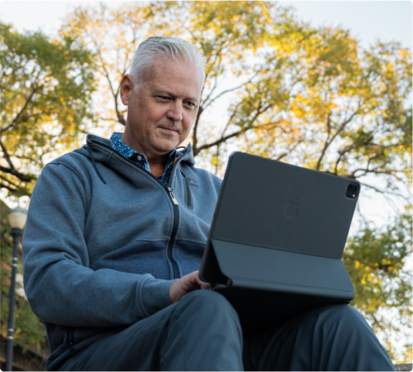 A middle-aged man working intently on a tablet outdoors