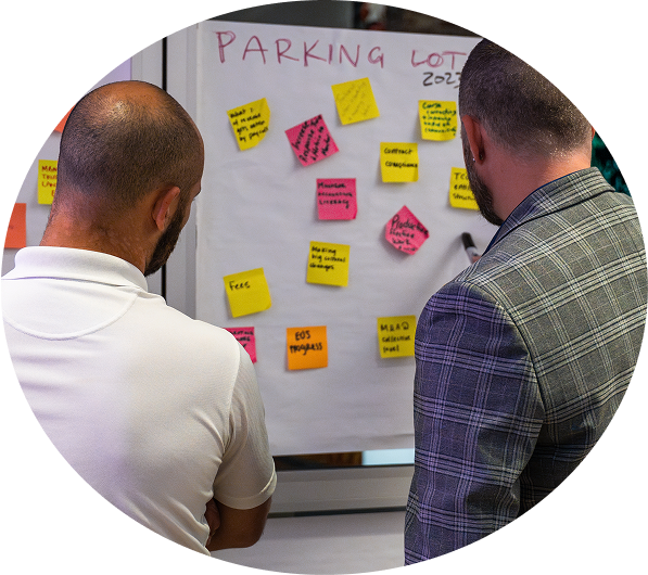 Two men closely reviewing sticky notes on a whiteboard