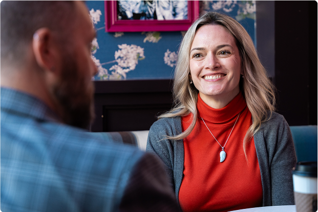 A woman smiling at a man from across the table in a coffee shop