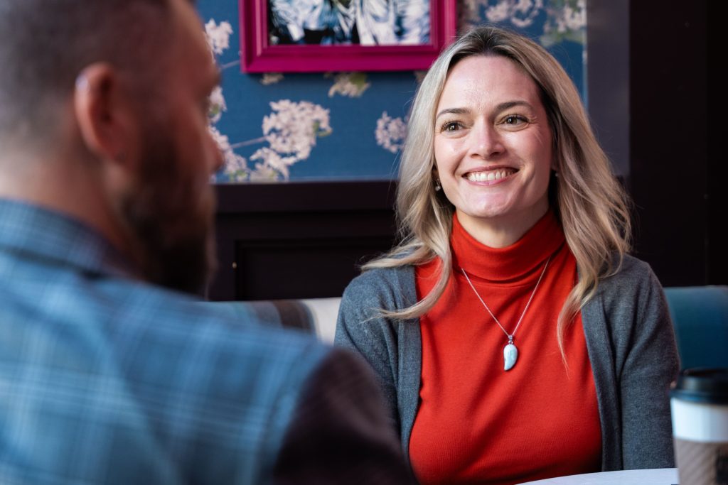 A woman smiling at a man from across the table in a coffee shop