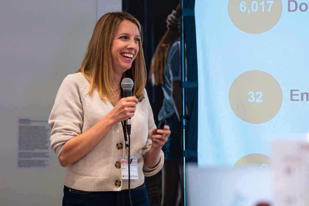 A smiling woman with a microphone presenting in front of a projector